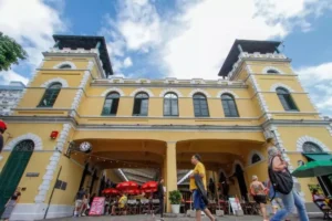 Fachada frontal do Mercado Público de Florianópolis, com suas torres e arcos, em dia ensolarado, com pessoas circulando.