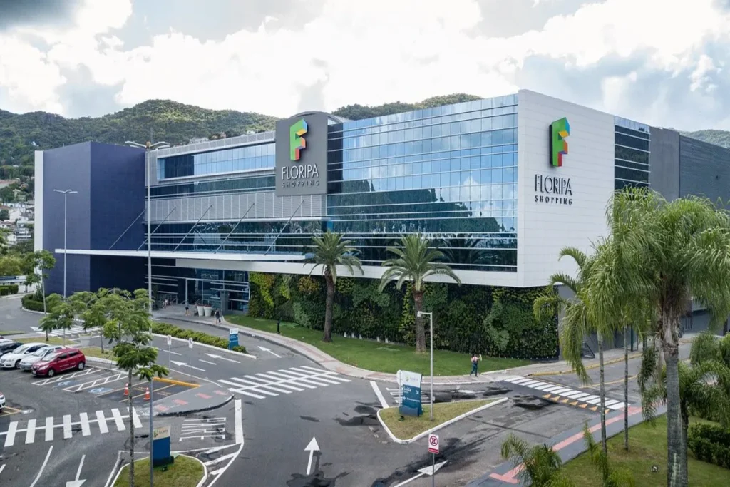 Vista externa moderna do Floripa Shopping em Florianópolis, com fachada de vidro, vegetação vertical e estacionamento. Centro de compras na ilha.