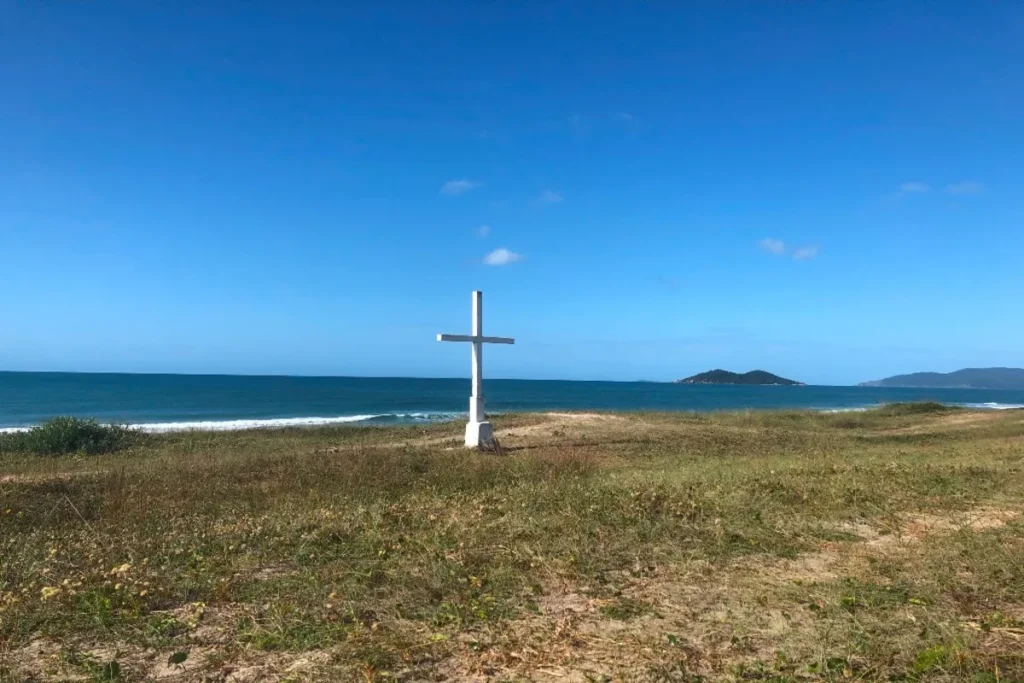Vista aérea da longa praia do Rio Tavares, com areia, ondas do mar, dunas e um caminho que leva às casas.