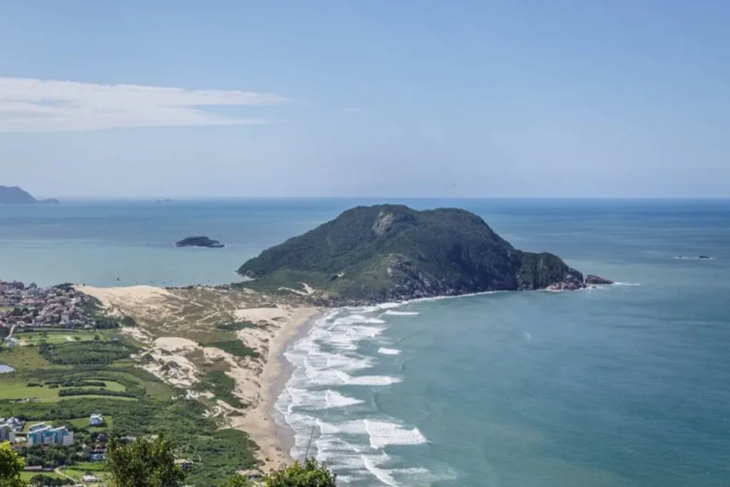 Vista aérea da Praia da Joaquina e do Morro da Joaquina, conectados por dunas de areia, em Florianópolis.