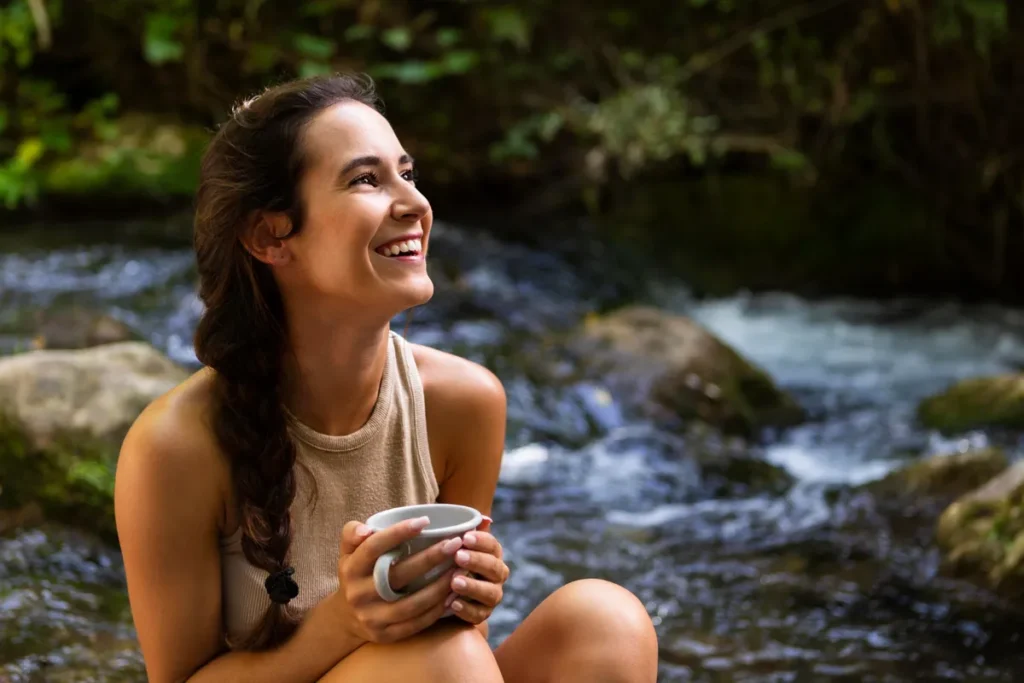 Mulher sorridente tomando chá ao lado de um rio em meio às cachoeiras de Florianópolis