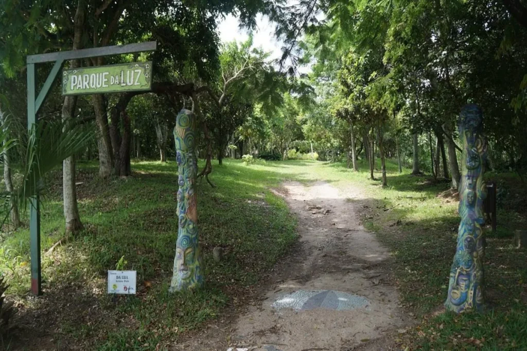 Entrada para o Parque da Luz em Florianópolis, com placa, caminho de terra e árvores.