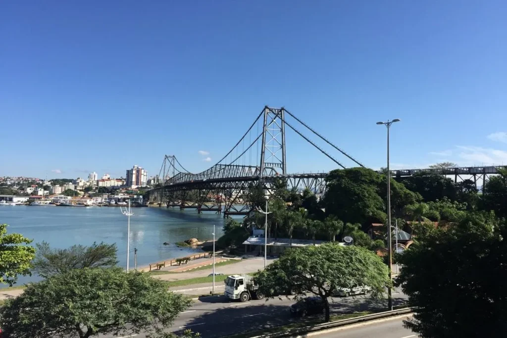 Ponte Hercílio Luz em Florianópolis em um dia ensolarado de céu azul, com vista da orla e prédios.