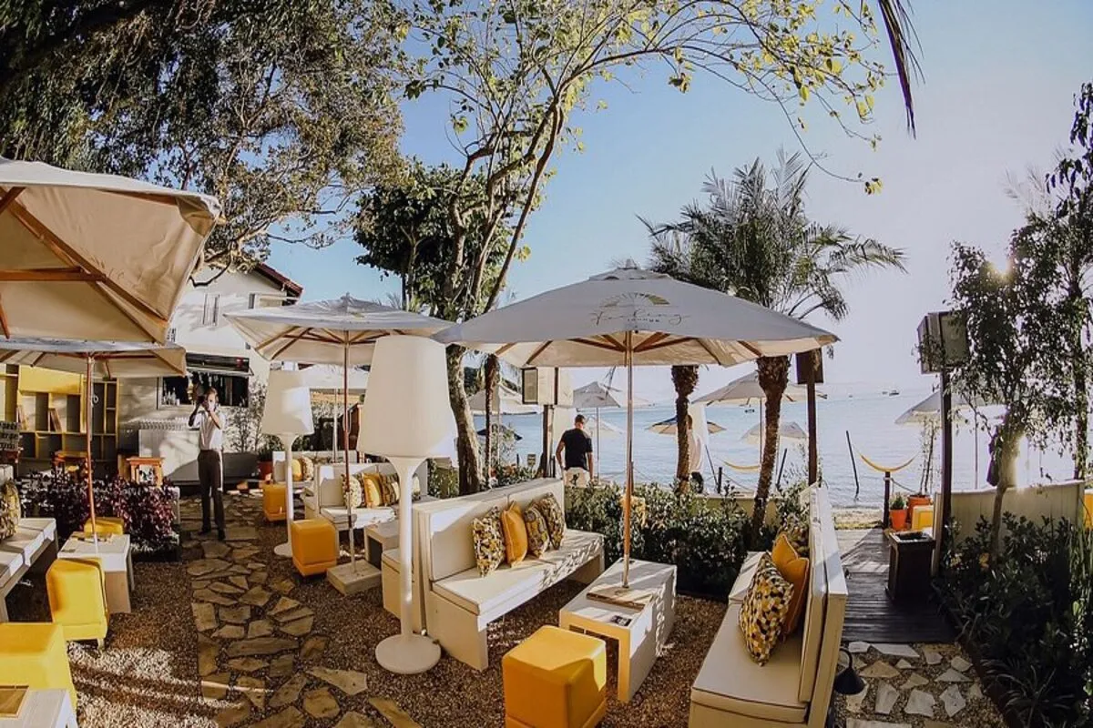 Área de lounge de um restaurante à beira-mar em Santo Antônio de Lisboa, com sofás brancos, almofadas amarelas e guarda-sóis.