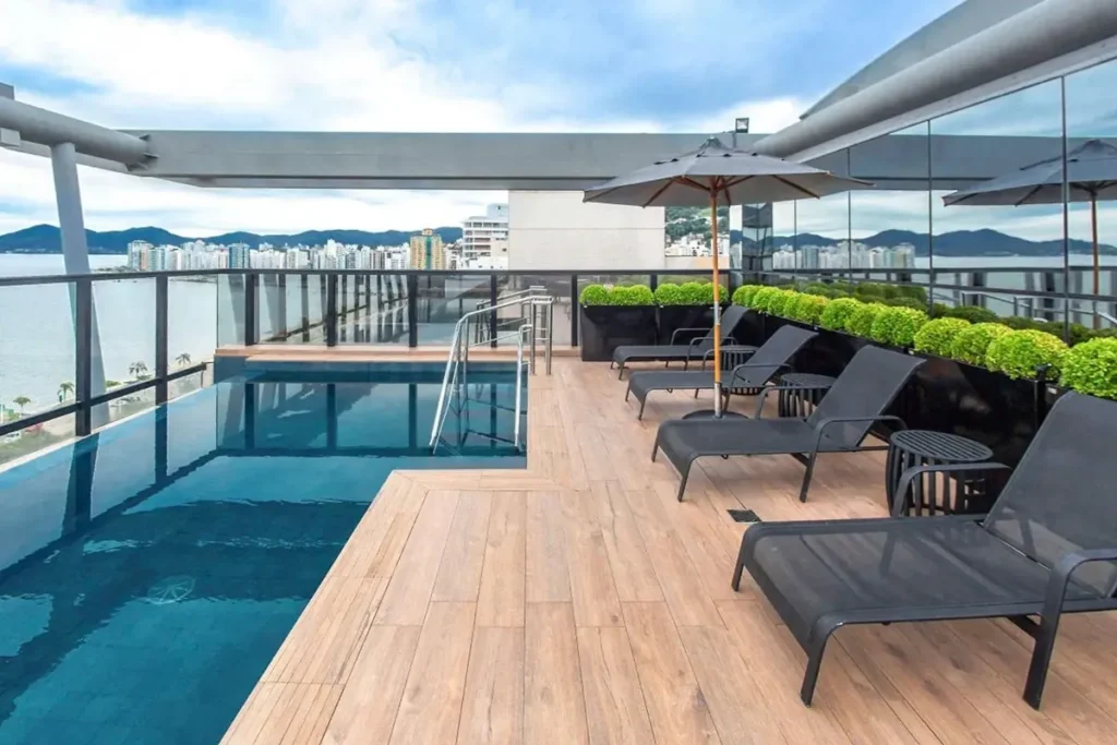 Piscina na cobertura do Hotel Novotel Florianópolis com vista para o mar e espreguiçadeiras dispostas sob guarda-sóis.