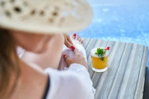 Mulher perto de piscina de hotel, com um drink do lado