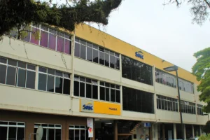 Fachada do Sesc Prainha em Florianópolis, prédio de três andares com janelas amplas, letreiro amarelo e áreas externas com vegetação.